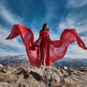 woman in red dress sitting on brown rock under blue sky during daytime