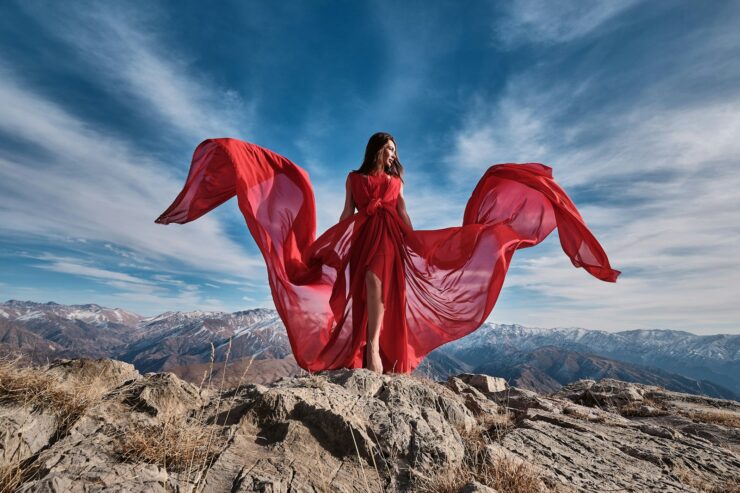 woman in red dress sitting on brown rock under blue sky during daytime
