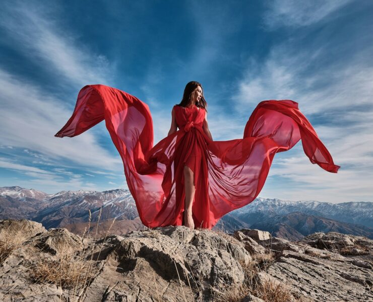 woman in red dress sitting on brown rock under blue sky during daytime