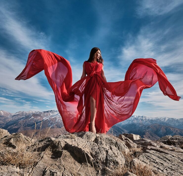 woman in red dress sitting on brown rock under blue sky during daytime