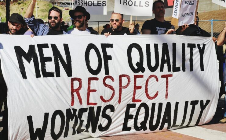 men holding white, black, and red Men of quality respect womens equality banner on road